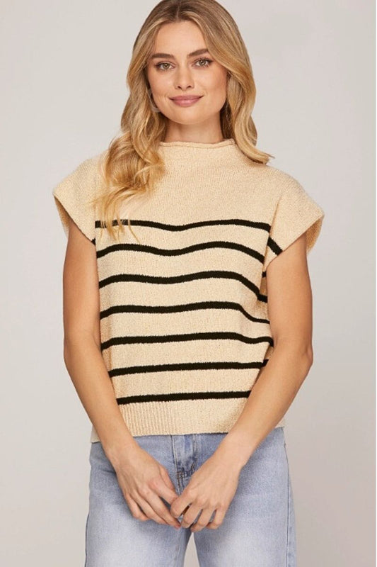 Woman wearing a beige sleeveless sweater with black stripes and light blue jeans on a plain background
