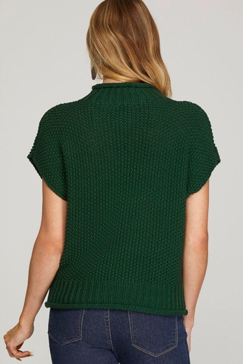 Person wearing a green knitted vest on a plain background