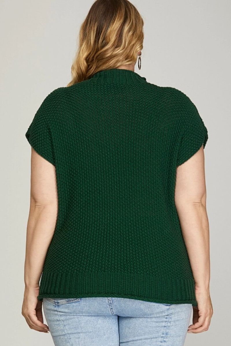 Person wearing a green knitted top with short sleeves on a plain background