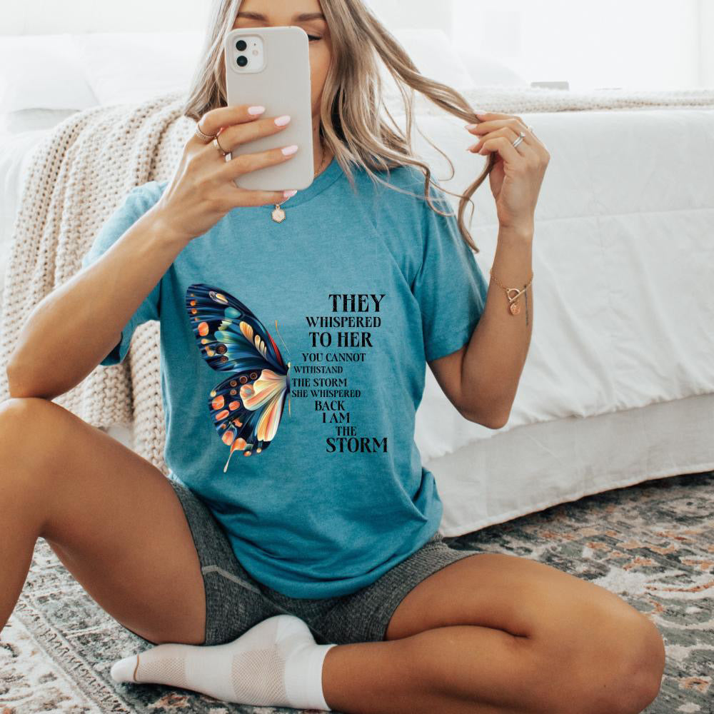 Woman wearing a blue t-shirt with a butterfly graphic and text, sitting on a couch.